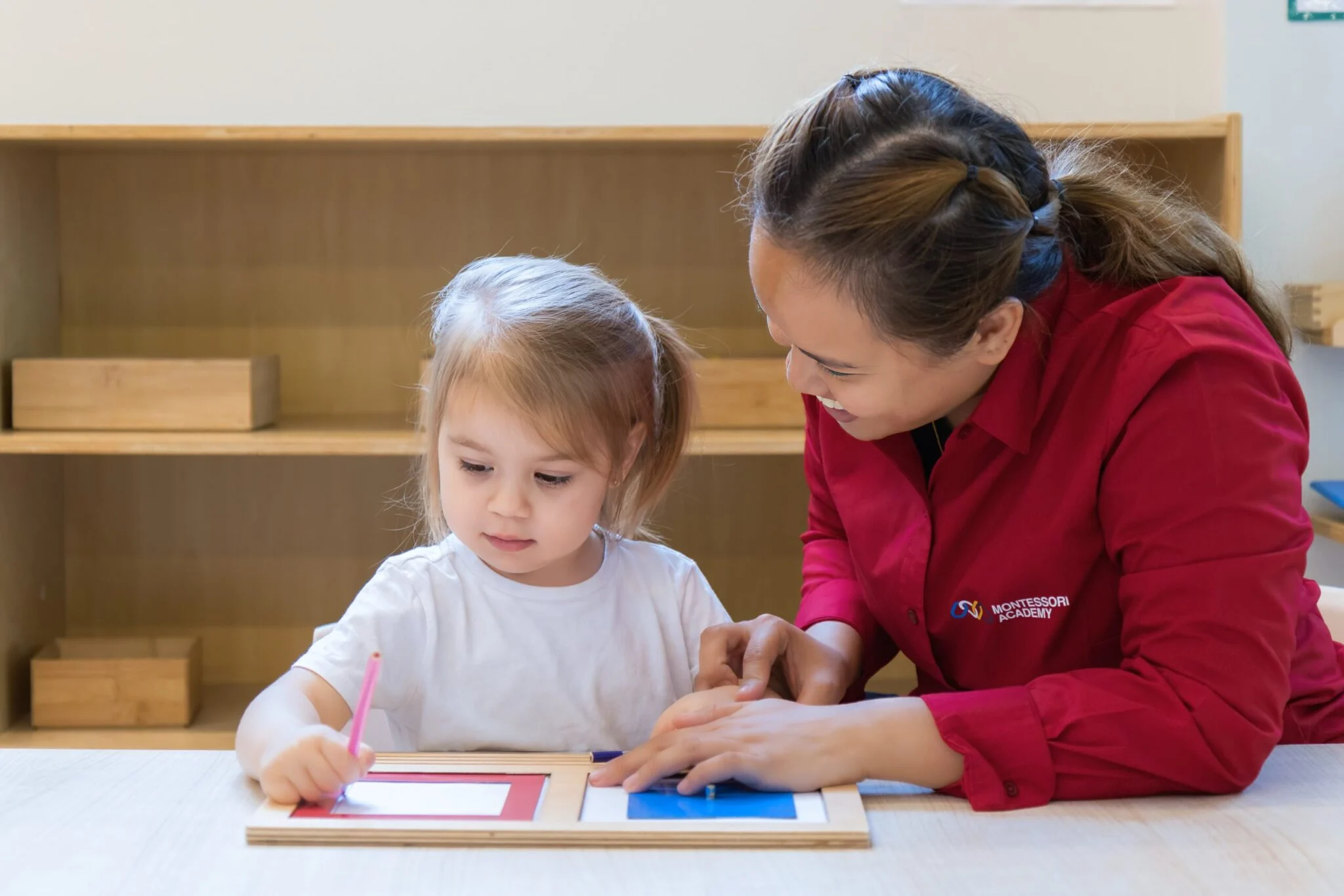 Montessori educator guiding a young child with a hands-on learning activity at a Montessori Academy classroom.