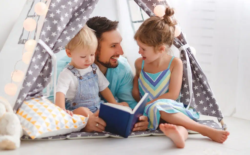 Father supporting early literacy development at home by reading to his two children