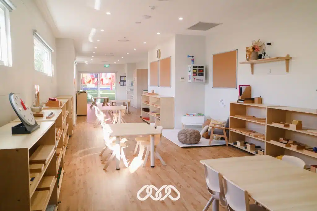Montessori childcare classroom with open shelving and children's tables and chairs