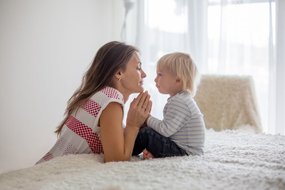 Montessori approach to discipline: image of mother And Toddler Boy Sitting On The Bed and Holding hands and looking at each other with love and respect