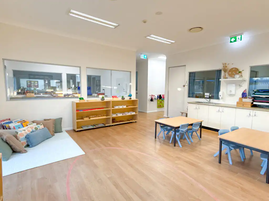 Montessori classroom at Auburn Albert Road childcare with tables, low shelves, kitchen area and quiet reading corner