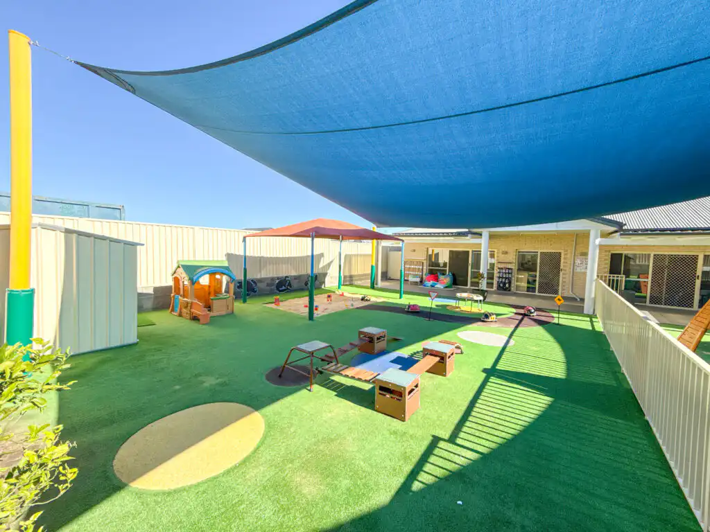 Outdoor Montessori play area at Auburn Albert Road childcare with shade sail, playhouse, sensory stations and open turf space