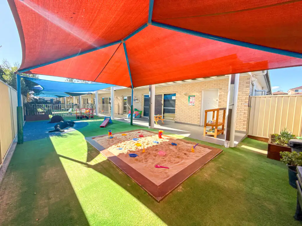 Sandpit play area at Auburn Albert Road Montessori childcare with shade sails, outdoor toys and artificial grass