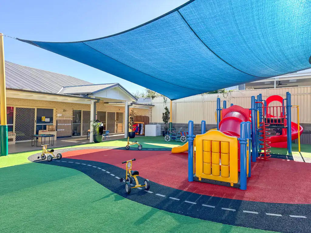 Outdoor Montessori playground at Auburn Albert Road childcare with slides, tricycles, shade sail and soft play surface