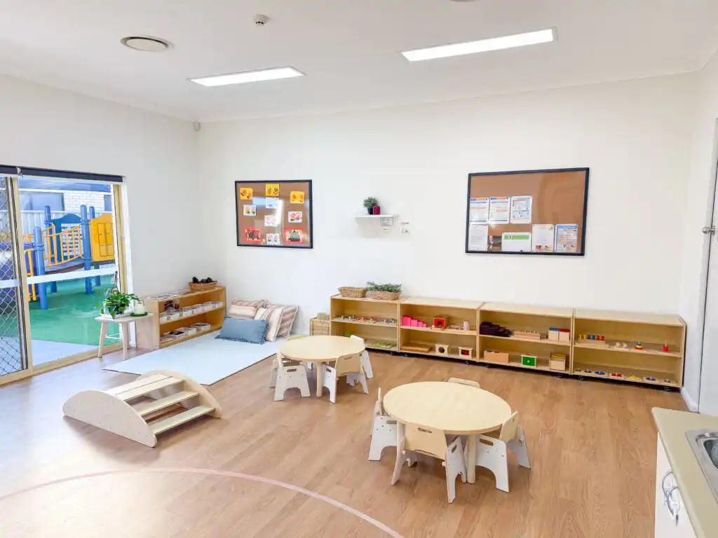 Montessori classroom at Auburn Albert Road childcare with round tables, balance ramp, learning shelves and outdoor view