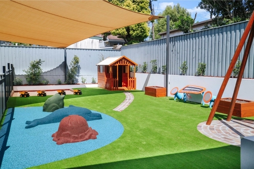 Outdoor play area at Auburn West Montessori Academy with cubby house, sandpit and open play space