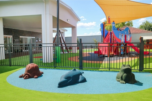 Outdoor play area at Auburn West Montessori Academy with soft-fall animals and shaded playground
