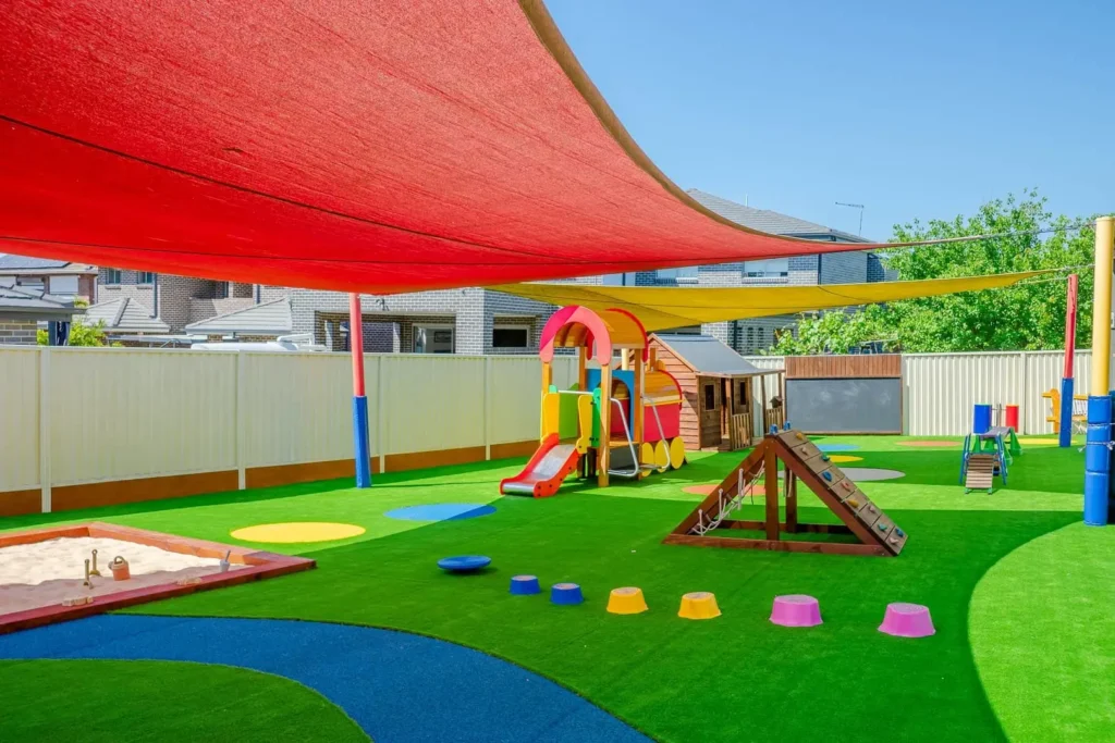 This Montessori Academy outdoor play area in Condell Park features shaded playground space, a sandpit, slide, climbing equipment, soft-fall surfacing, and open areas designed to support coordination, confidence, movement, and hands-on early learning.