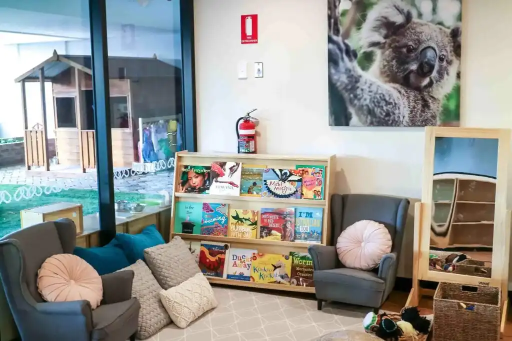 Montessori reading corner at Crows Nest childcare with book display, armchairs, cushions and outdoor play area view