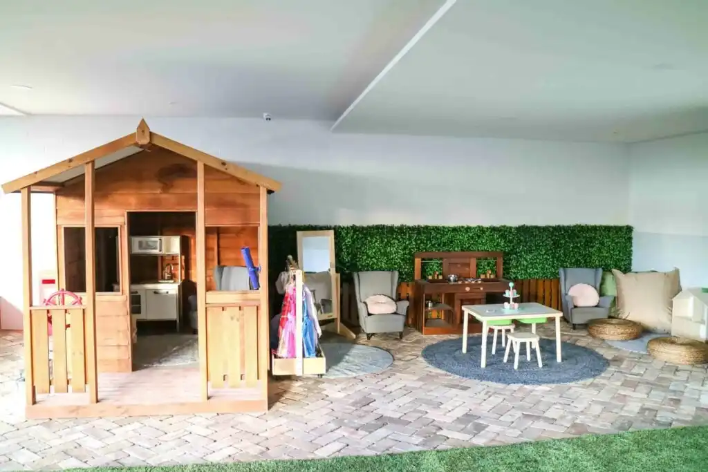 Indoor outdoor Montessori play area at Crows Nest childcare with wooden cubby house, home corner setup, table and seating