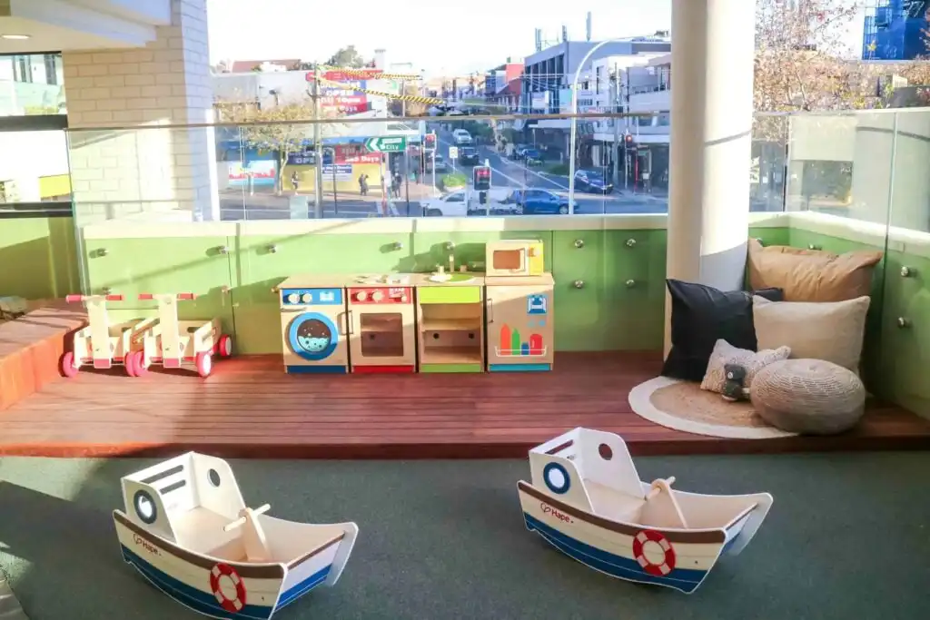 Outdoor balcony play area at Crows Nest Montessori childcare with play kitchen, toys and city street views