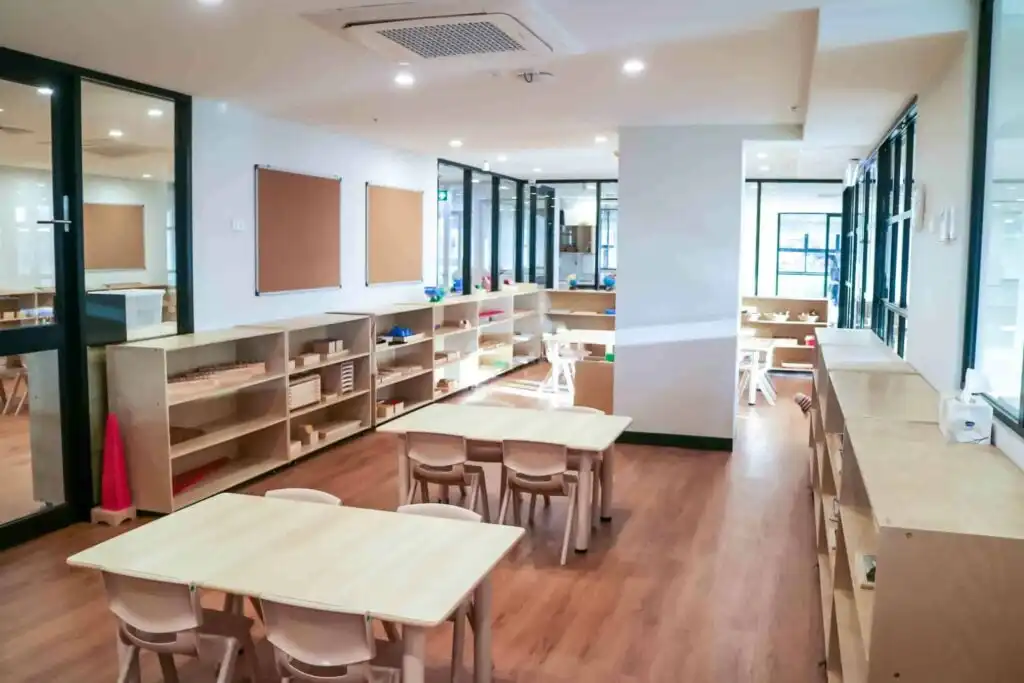 Montessori classroom at Crows Nest childcare with wooden tables, low shelves and glass connected learning areas