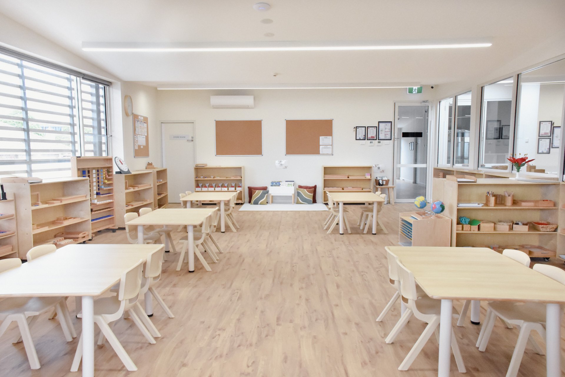 Childcare Montessori Preschool Classroom with open shelving, desks and chairs, and Montessori materials.