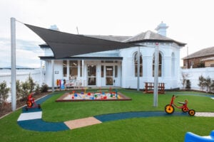 Childcare outdoor playground with sandpit, bike track, tricycles, and shade sails