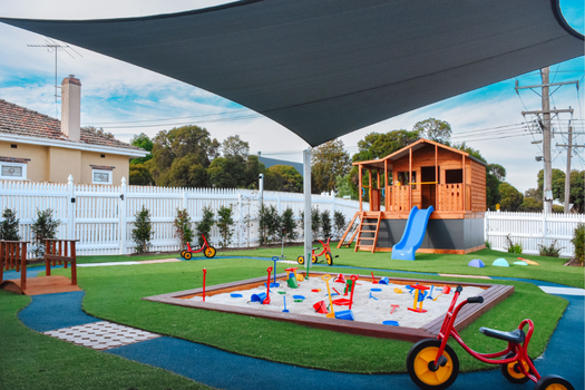 Outdoor play area with sandpit, cubby house, slide, and shaded play spaces at Elsternwick Montessori Academy.