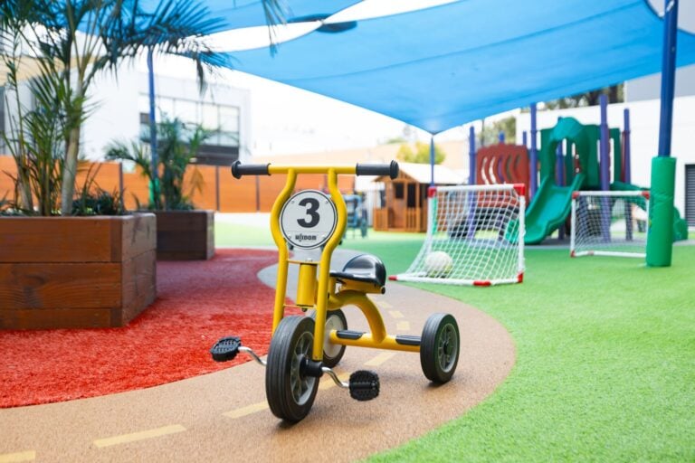 Shaded outdoor play area at Entrada Parramatta childcare centre with tricycle path, slide and soccer goals