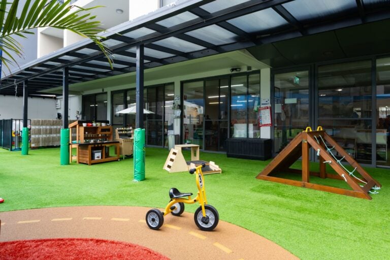 Shaded outdoor play area at Entrada Parramatta childcare centre with climbing frame and tricycle path