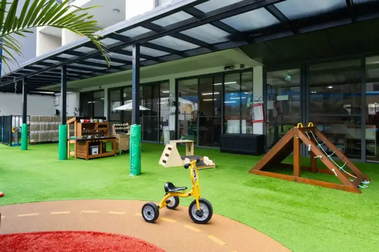 Shaded outdoor play area at Entrada Parramatta childcare centre with climbing frame and tricycle path