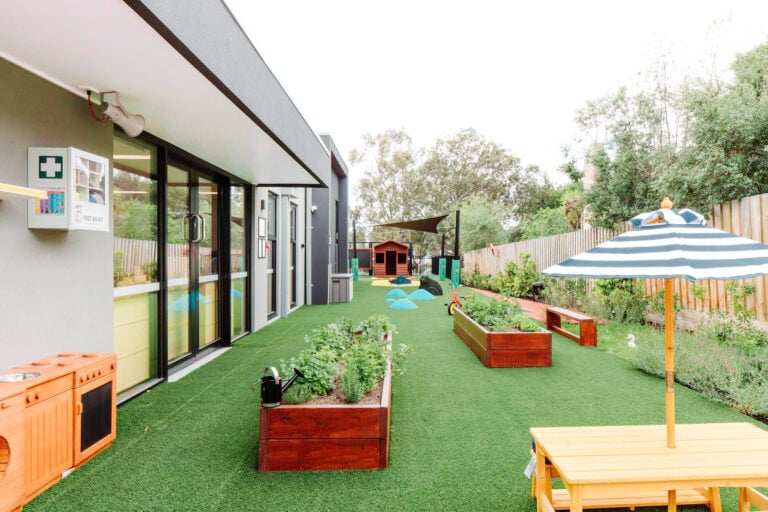 Outdoor area of Montessori Academy’s Templestowe childcare, with two garden plots, turfed play areas and an outdoor table.