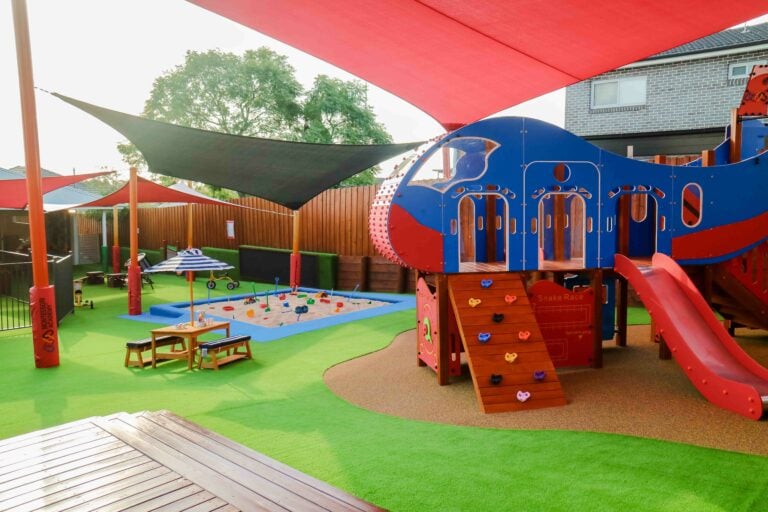 Outdoor playground at Guildford Montessori Academy, with play areas, a playhouse, slide, climbing ramp, and sand pit.