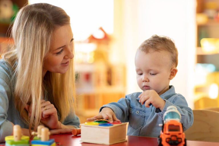 A mom teaching her toddler to use a wooden colour box to learn colour matching.