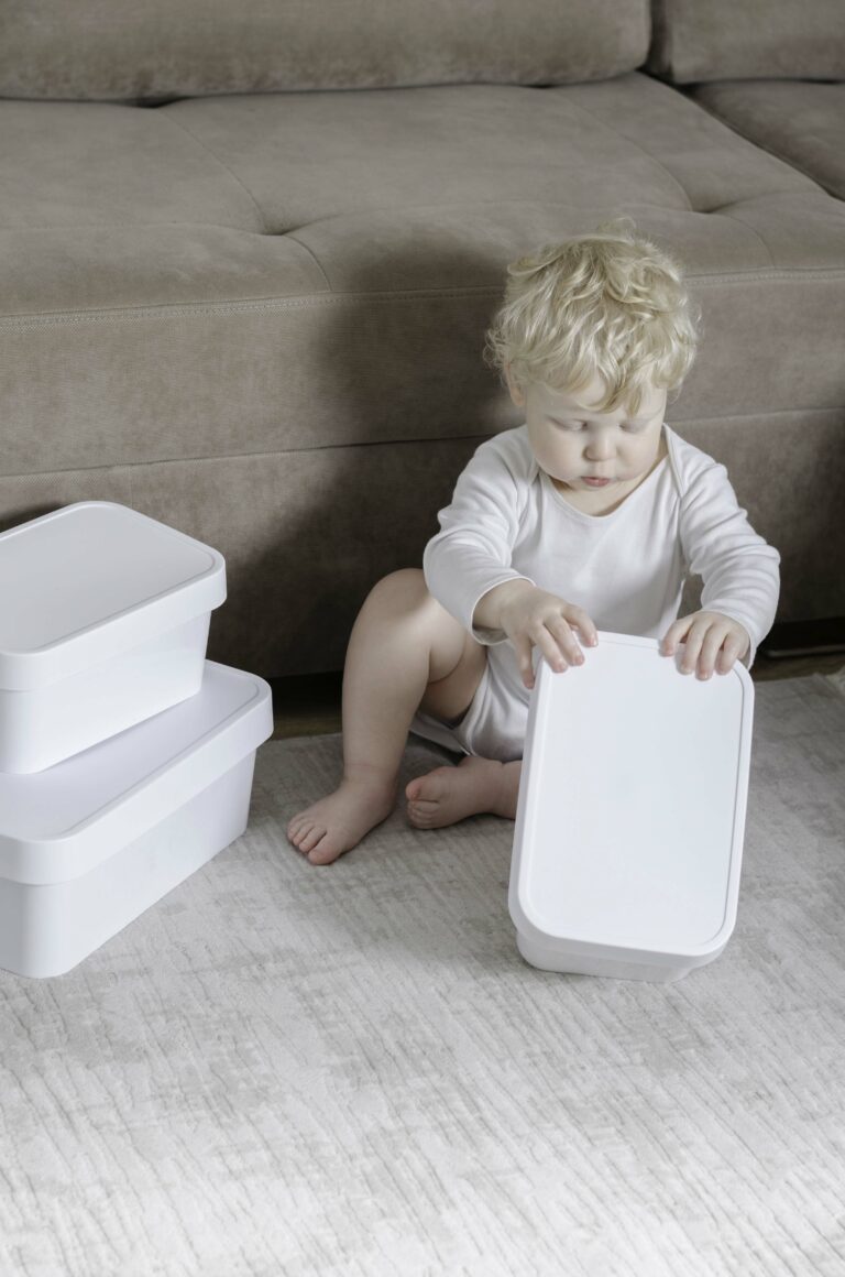 A toddler sat down on a carpet floor trying to open a white box.