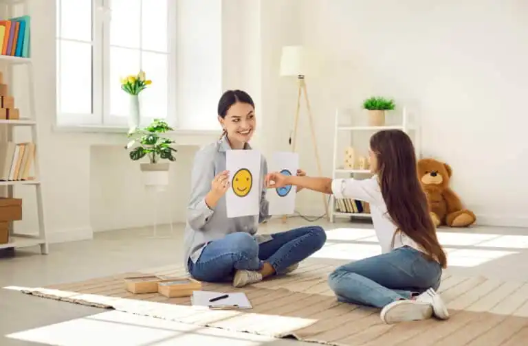 Aw oman holding a smiling and frowing faces on paper and young girl pointing to the smiling face