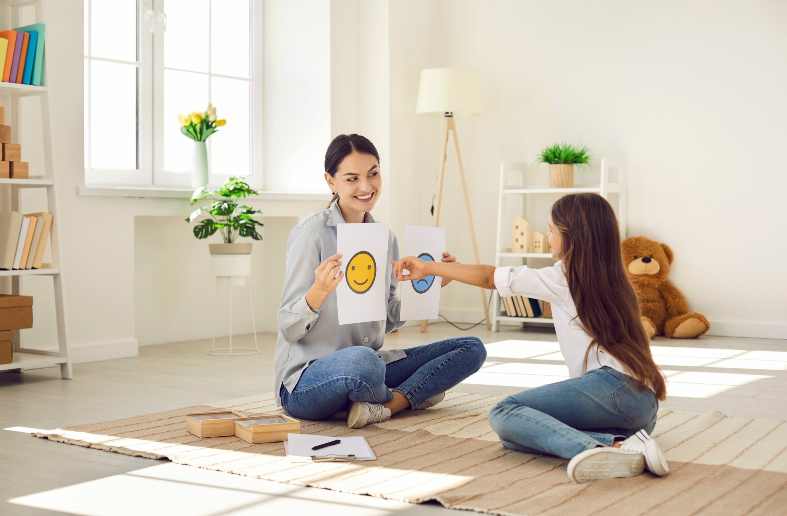 Aw oman holding a smiling and frowing faces on paper and young girl pointing to the smiling face