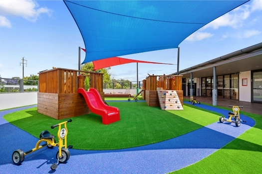 Shaded outdoor playground at Penrith Derby Street Montessori Academy with slide, climbing equipment and tricycles