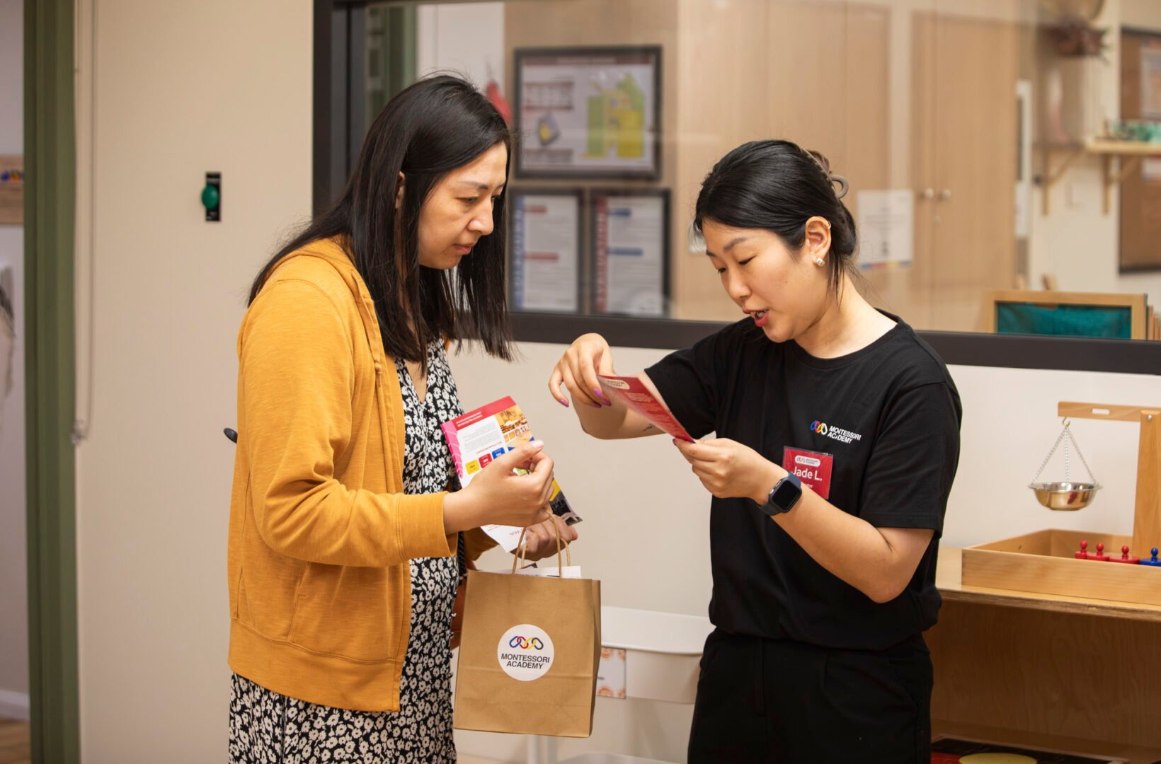An educator warmly speaks with a parent who is holding a gift bag filled with brochures about the childcare centre.