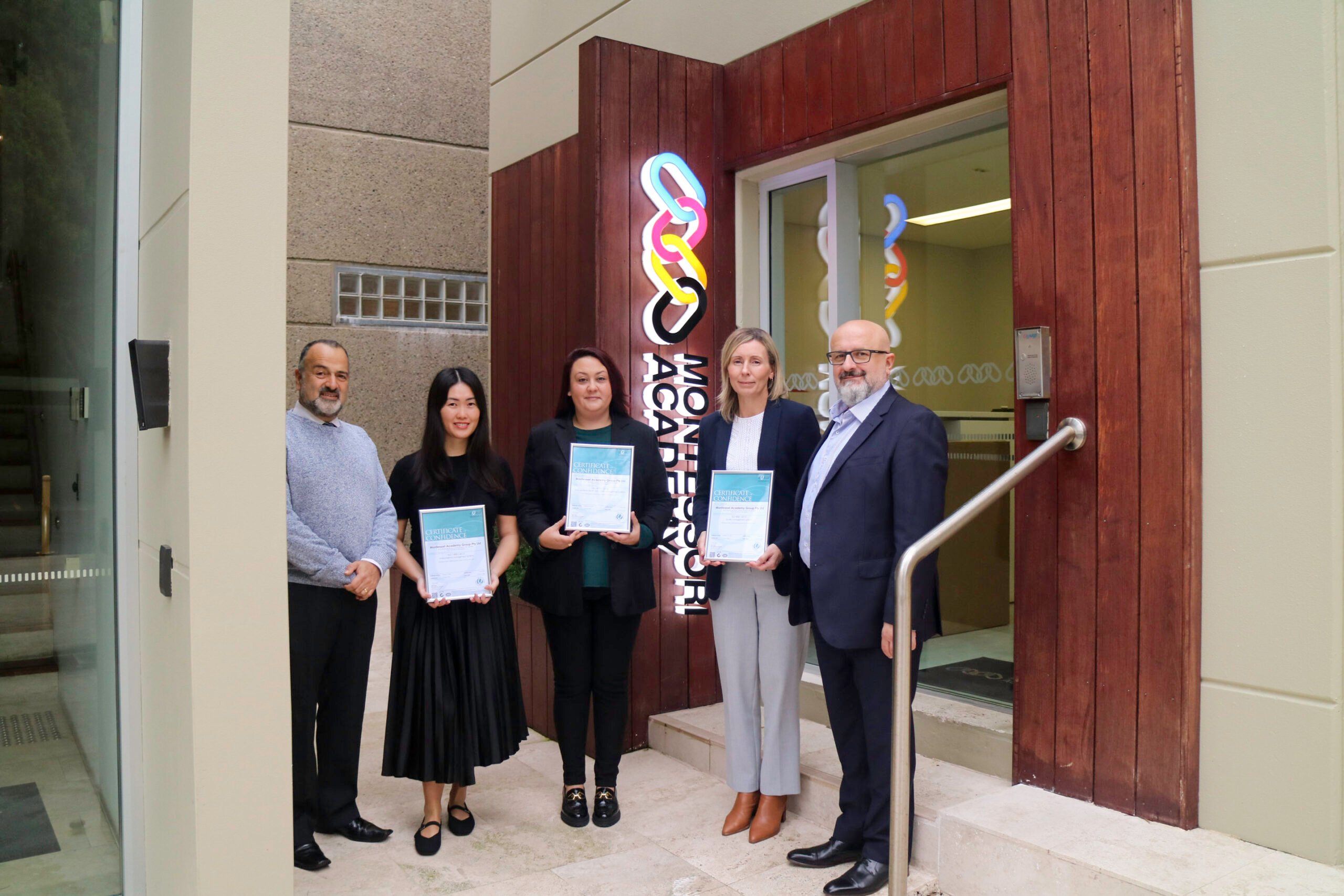 A diverse team of senior leaders stand in front of a Montessori Academy logo