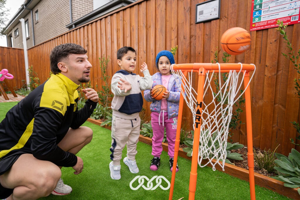 Children playing child sized basketball with the supervision of sports instructor outdoors at grand opening of Condell Park North Montessori Academy.