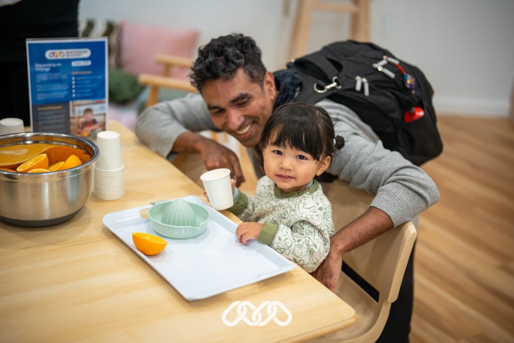 Child and parent enjoys Montessori practical life orange squeezing activity at St Marys grand opening event in preschool room.