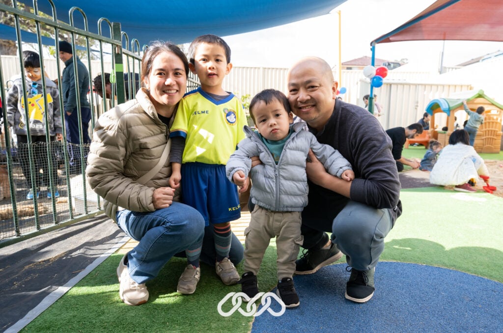 Family of four poses together for a photo in the outdoor toddler area of Montessori Academy Auburn at an Open Day