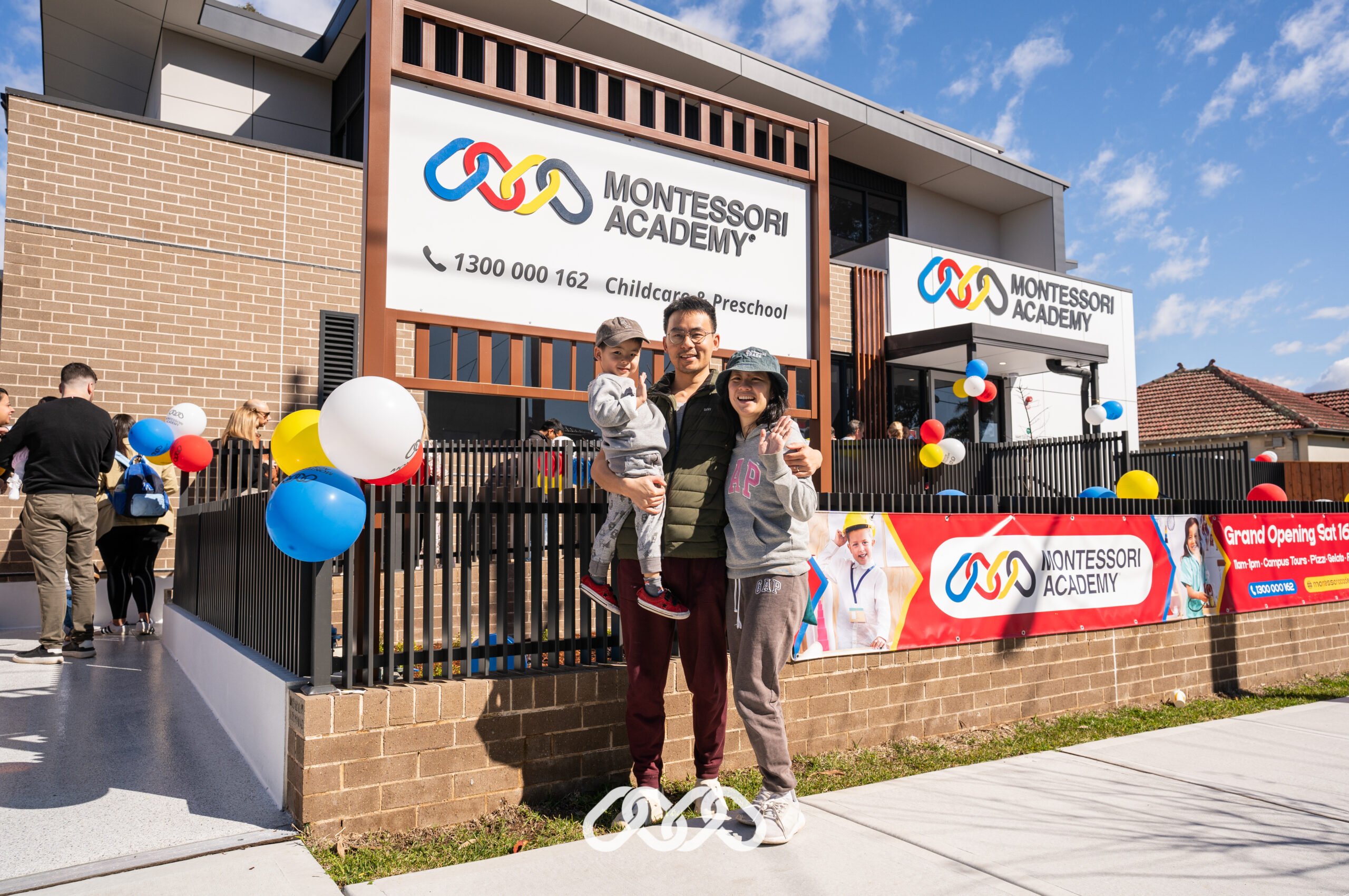 Family poses in front of Bexley Montessori Academy at the Grand Opening of the centre with colourful balloons and banner.