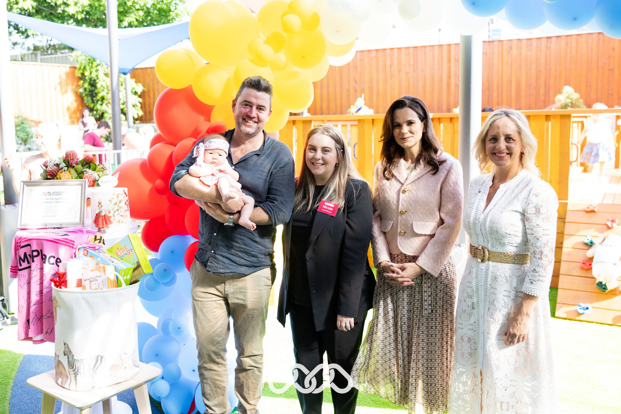 Giveaway hamper winner, senior leadership and MP gathered around balloon arch.