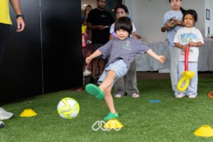 Child kicks small soccer ball in outdoor area at Riverwood Montessori Academy Grand Opening