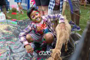 Child with tiger face paint pats at goat at in outdoor area at Riverwood Grand Opening