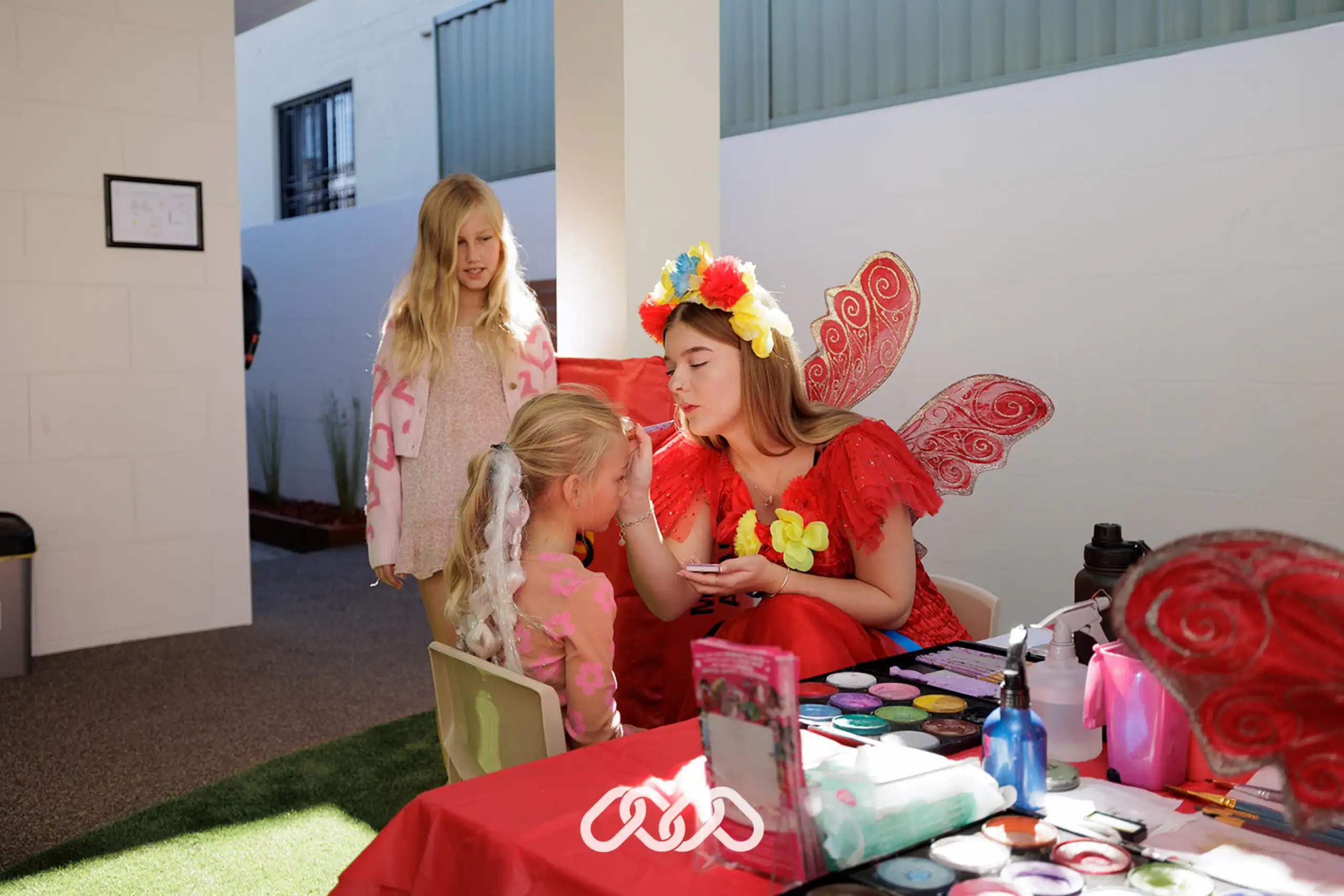 Blonde child gets face painted by adult dressed in red fairy costume at Hurstville Grand Opening