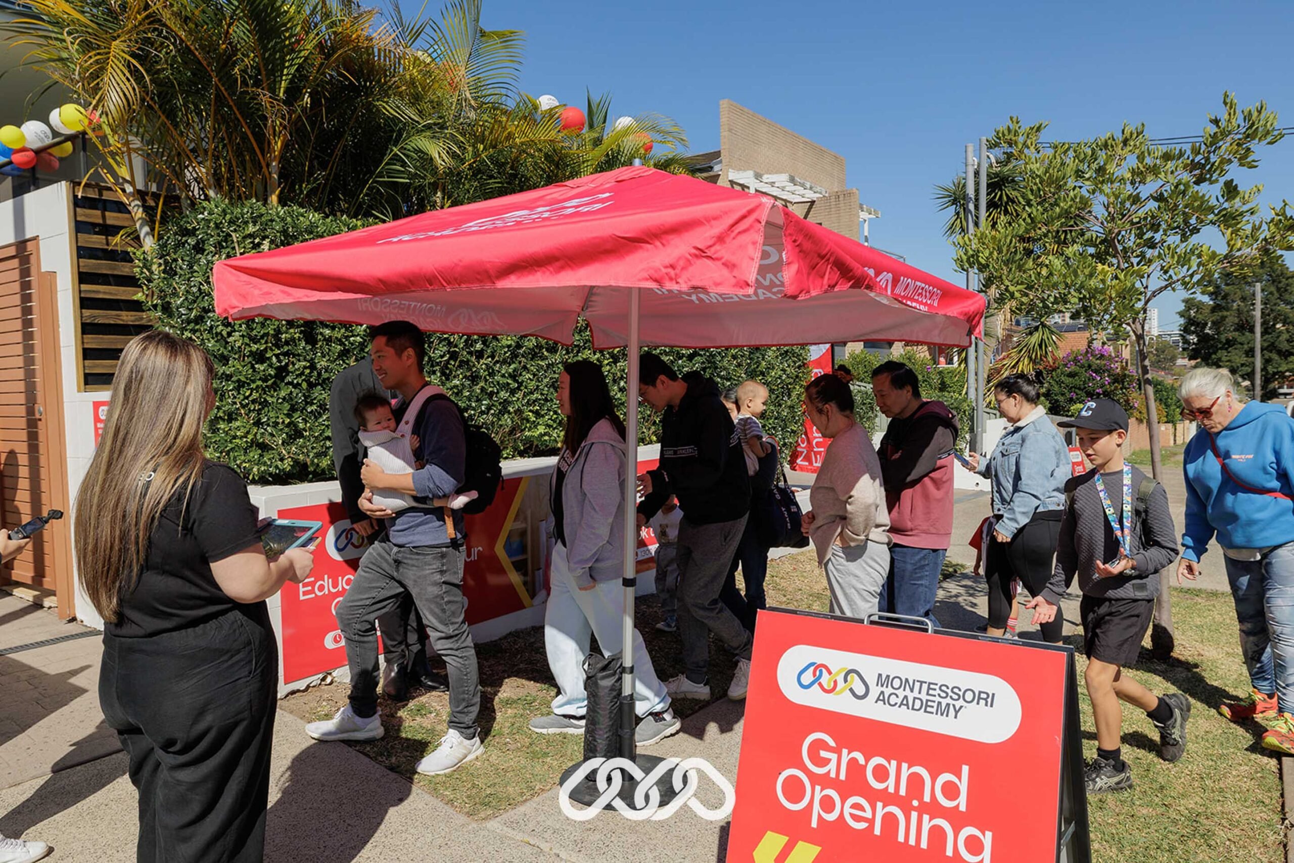 Families waiting outside under red umbrella to enter the Hurstville Montessori Academy grand opening event