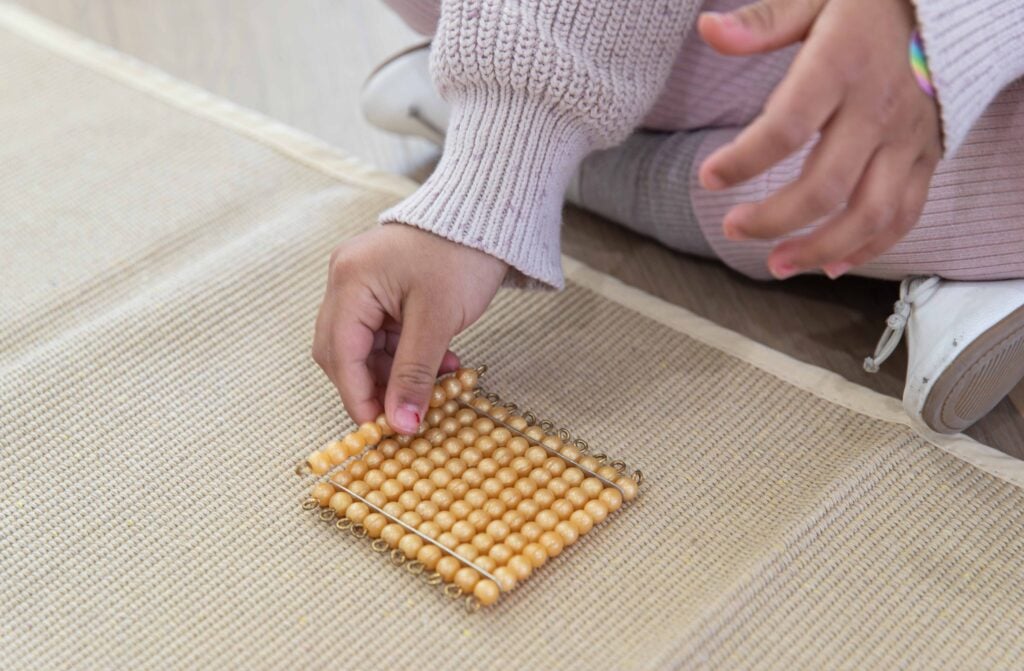 A child using Montessori golden bead materials to explore the decimal system and place value as part of early numeracy learning.
