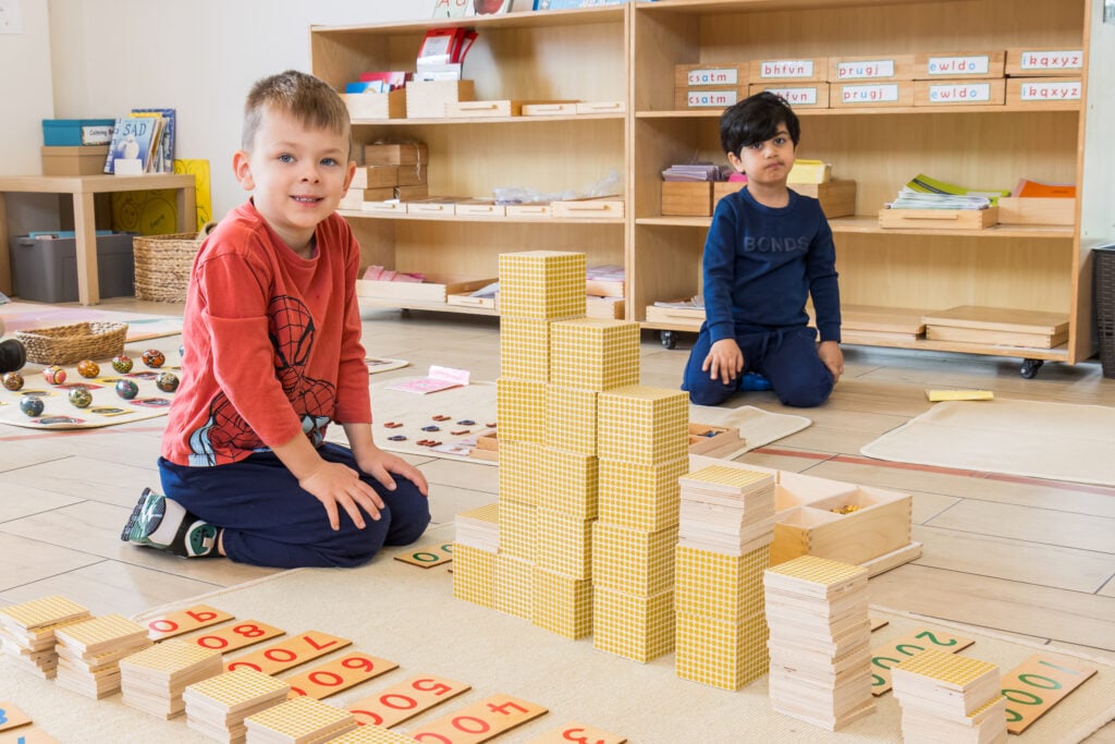 Children using Montessori Seguin Boards and golden bead materials to explore teen and tens numbers as part of early numeracy learning.