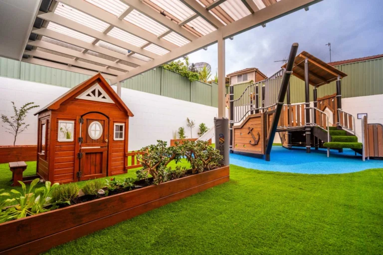 Outdoor play area with wooden cubby house and pirate ship fort.
