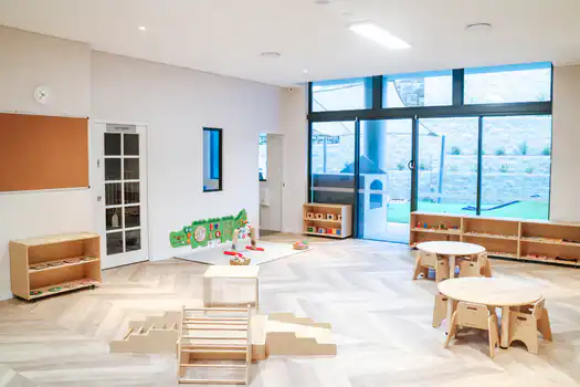 Bright infant Montessori classroom at Lane Cove West Montessori Academy featuring natural timber furniture, open floor space, Montessori learning materials, and large windows with direct access to the outdoor play area.