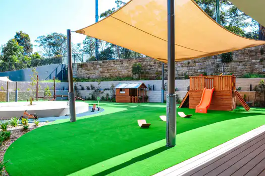 Outdoor playground at Lane Cove West Montessori Academy featuring shaded play areas, climbing equipment, cubby house, slide, and open green spaces for active exploration.