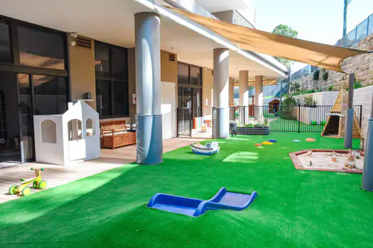 Outdoor play area at Lane Cove West Montessori Academy featuring shaded learning spaces, soft fall surfaces, sandpit play, cubby house, and open-ended outdoor activities for young children.