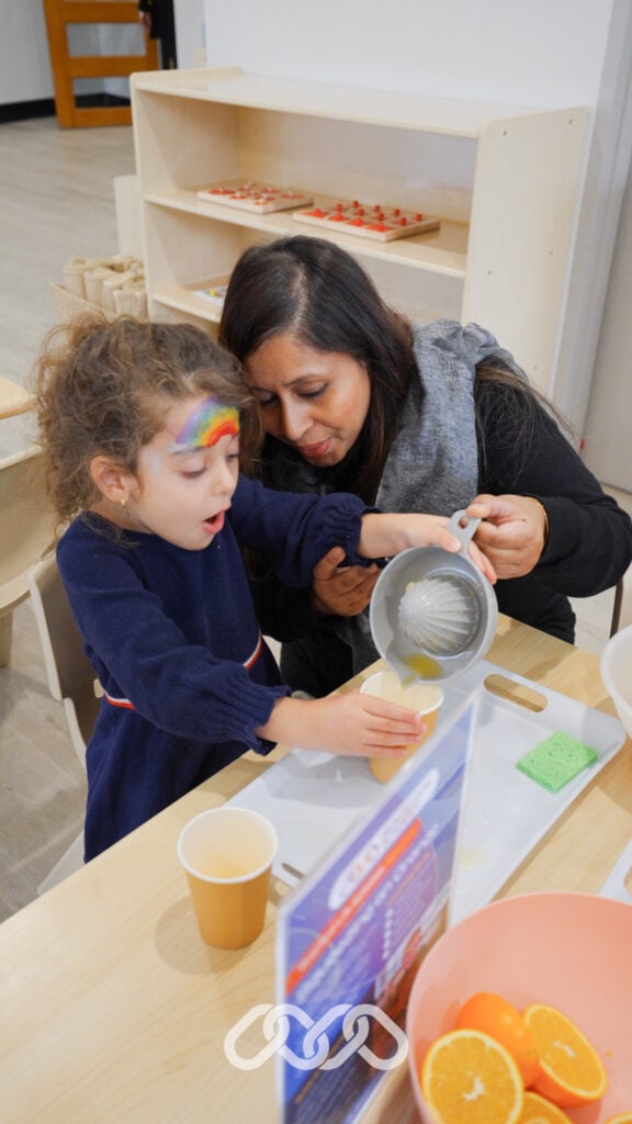 child tips juice from orange squeezer into a cup with assistance of educator