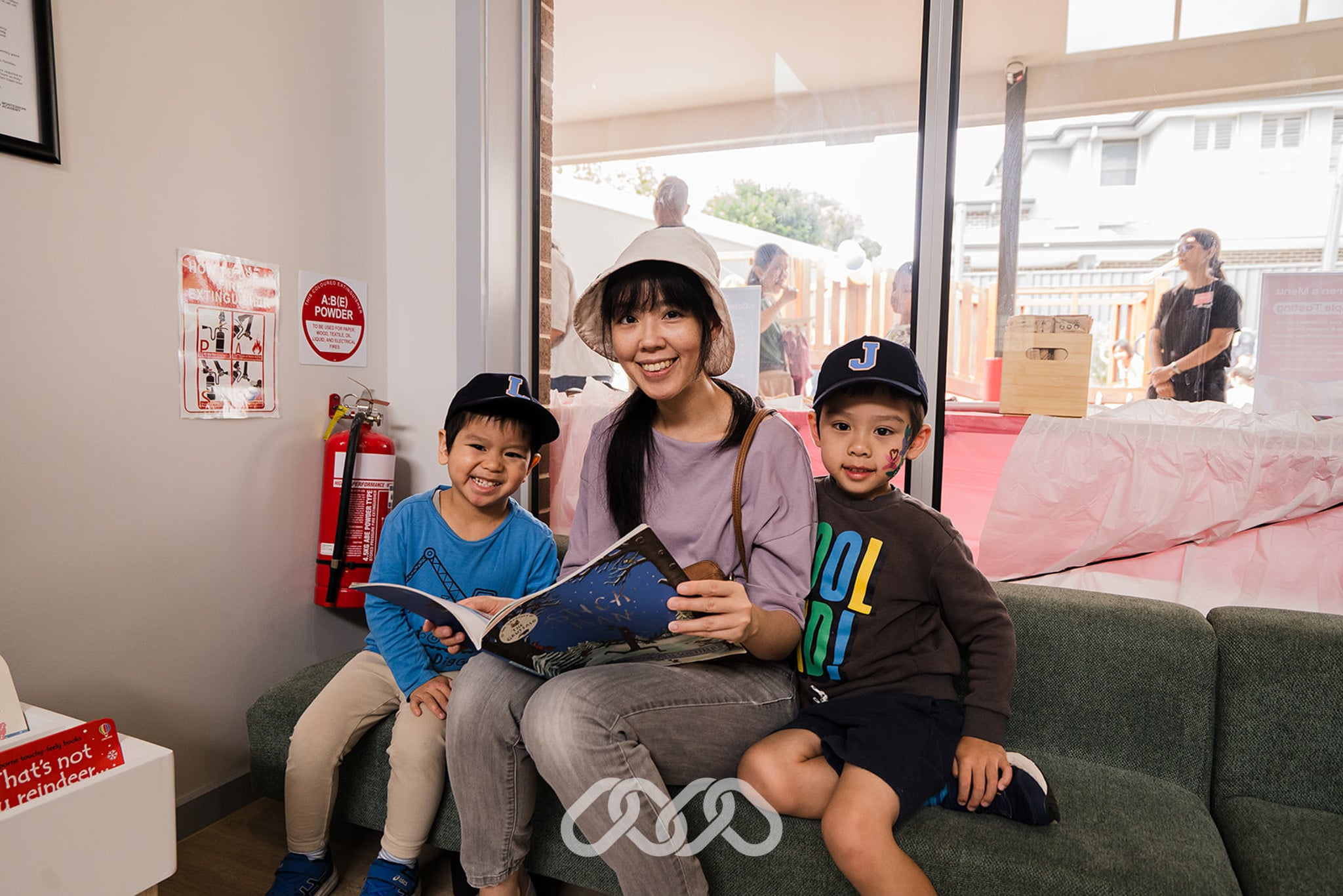 Mother sits with her sons on a green couch and holds a book as she reads them a story
