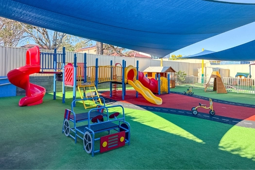 Outdoor playground at Auburn Montessori Academy with slides, shade sails and ride-on play equipment