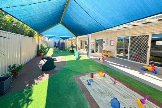 Shaded outdoor play area at Auburn Montessori Academy with sandpit and open play space